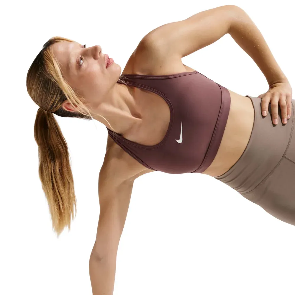 Mulher loira usando top esportivo marrom Nike, segurando garrafa de água
